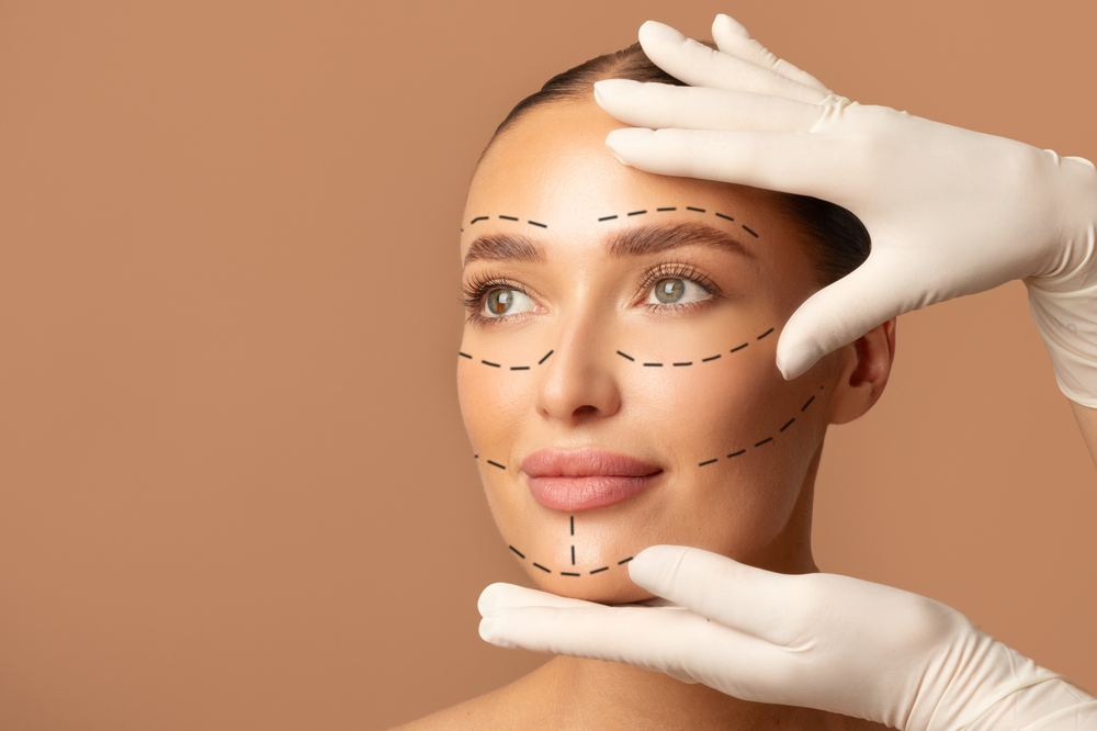 PortraitOfYoungWomanAndPlasticSurgeonMakingMarksOn - Dr Leena Jain Woman's face with dashed surgical markings for cosmetic contouring, gloved hands around the jaw and chin area.