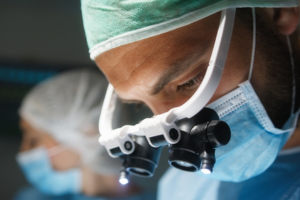 Untitled-design-21 - Dr Leena Jain Surgeon wearing surgical loupes and mask, focused on a procedure in a bright operating room.